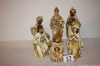 Front view of all six colorful nativity figurines arranged in a group, painted with mainly gold and cream colors, featuring baby Jesus, Mary, Joseph, and three kings.