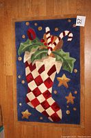 Full view of rectangular stocking rug with holiday design on wooden floor.
