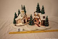 Overview of entire ceramic Christmas village showing lighted church, houses, and trees on base with ruler for scale