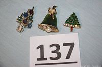 Three vintage holiday brooches including a colorful tree, green bell with pearl, and rhinestone tree