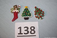 Set of three vintage holiday brooches on white background with lot number 138 visible