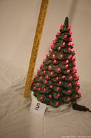 Front view of vintage green ceramic Christmas tree illuminated with red light bulbs, next to a measuring stick showing height.