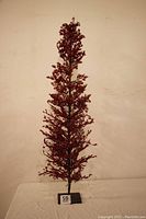 Full view of the tall, slender Christmas tree decorated with red crystals on branches, standing on a white surface against a plain wall.
