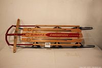 Full side view of the vintage wooden sled showing branding and metal runners.