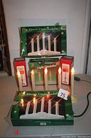 Lot with electric 5 light and 3 light window candles lit on a table, showing bulbs glowing and packaging
