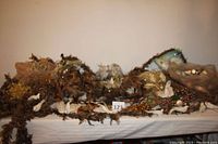 Wide shot of assorted woodland creature and nature-themed Christmas tree decorations spread out on a white tablecloth with multiple nests, feather garlands, pine cones, and glitter fruit ornaments.