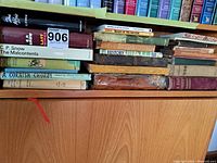 Photo of assorted antique and vintage books stacked horizontally on a shelf, showing titles and various cover styles.