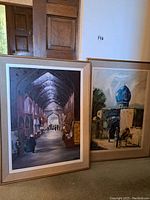 Photo showing both framed oil paintings, one depicting an indoor market and the other a blue-domed structure.