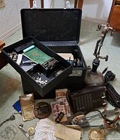 Open black metal carry case with removable tray containing assorted small hardware items and visible quill pen nibs