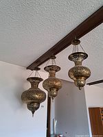Three brass hanging lanterns suspended from a wooden ceiling beam