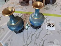 Two medium-sized blue cloisonné vases on black wooden stands flanking a smaller white cloisonné vase on a table.