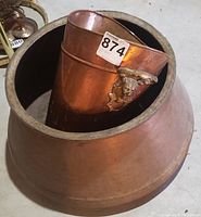 Two copper planters, one nested inside the other, showing the larger conical planter and the smaller planter with lion head handles inside it.
