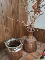 Wide shot showing both copper pots together, including floral arrangement in the taller pot