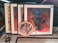 Four framed indigenous prints featuring Kwakiutl art and two small wooden carvings placed in front of them.