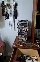 Photo shows necklaces hanging on a rack and assorted jewelry on a dresser surface including earrings and bangles.