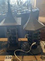 Two metal pagoda-style lanterns with colored glass inset on a table, cords visible, untested condition.