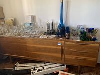 Full front view of the mid century wooden buffet with various glassware placed on top, showing two sliding cabinet doors and three drawers on the right side.