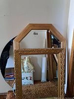 Multiple mirrors stacked against a wall including a round frameless mirror, an octagonal wood framed mirror, and a rectangular ornate framed mirror