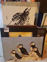 Various original bird artworks including a monochrome drawing and framed paintings of puffins and other birds.