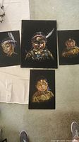 Four black velvet paintings arranged on floor showing Indigenous child portraits.