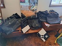 Wide shot of assorted black purses, various styles and sizes, plus one white and black clutch on a wooden surface