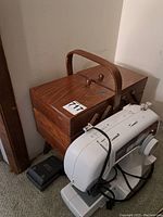 White Brother XL2600 sewing machine next to wooden sewing box on carpeted floor, sewing box has carry handle and is closed