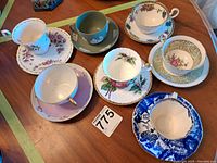 Photo showing eight assorted teacups and saucers on wooden table, displaying various patterns and colors.
