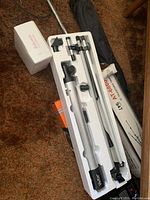 Vivitar refractor telescope and components in styrofoam packaging with accessories and tripods nearby on carpeted floor.
