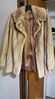Full view of vintage brown fur coat hanging on a hanger showing collar and lining.