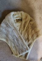 The beige fur stole folded on a surface showing texture and cream color.