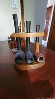 Three traditional-style smoking pipes on a rounded wooden rack, showing textured finishes and different colors.