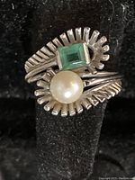 Front view on black stand showing pearl and emerald with geometric band design