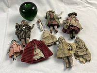 Group view of nine half dolls and accessories with green glass apple for scale