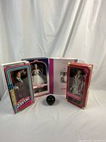 Overview of all four boxed Barbie dolls with green apple size reference