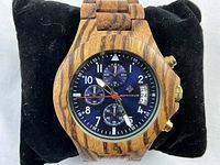 Close-up of Bonheur wrist watch with African zebra wood case and band, blue chronograph dial, red second hand, white numerals. Watch face shows date window.