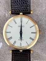 Close-up of watch face showing cream dial, black Roman numerals, black hands, "GUCCI" and "Quartz" markings on 31 mm case.