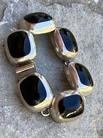 Close up of the bracelet showing the polished black jet stones set in thick silver bezels on a textured stone background.