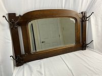 Oak Arts and Crafts antique framed mirror with four metal coat hooks, displayed laying flat on white background. Shows front view of the frame, mirror glass, and hooks.