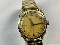 Front view of watch showing gold-tone textured dial, applied hour markers and Omega logo