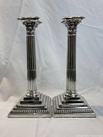 Front view of pair of tall silver plated Corinthian column candlesticks on stepped square bases