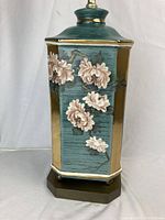 Close-up of hexagonal lamp base with hand-painted pink peony flowers, teal background, and gold accents on dark brown wooden platform.