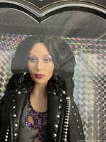 Close-up of doll head and torso showing face sculpt, curly dark hair, and studded faux leather coat