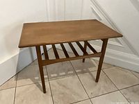 Full view of teak end table showing rectangular top and angled legs with lower slat shelf.
