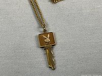 Close-up of 14k gold Playboy key pendant and 18-inch chain on fabric background