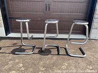 Three chrome cantilever stools arranged side by side showing overall design