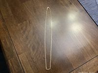 Full length view of 24-inch yellow gold chain necklace laid on wooden surface