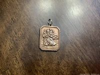Close-up front view of rectangular medal pendant on wood background.
