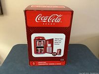 Photo of Coca-Cola cooler box showing product image and branding, indicating it holds 12 cans and is suitable for car, boat or home use.