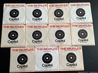 Photo showing all 11 Beatles original Capitol Records sleeves laid flat, each with black target logo and red band name.