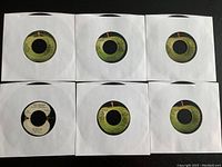 Photo showing 6 of the Beatles 45 RPM records in white paper sleeves, with visible record labels featuring The Beatles song titles and catalog numbers.